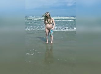 Pregnant blonde undresses at the beach